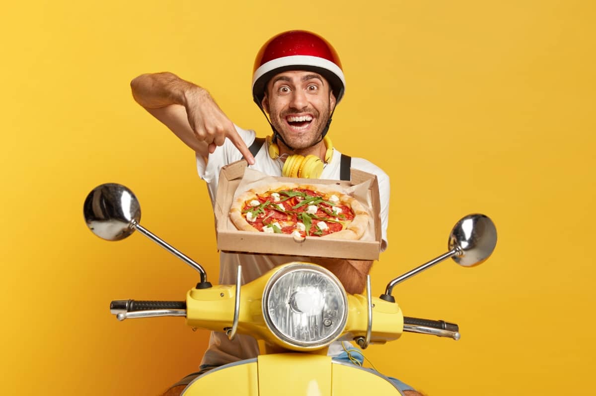 Persona feliz sobre motocicleta haciendo delivery de una pizza